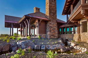 Back of property with a garden pond, a standing seam roof, a chimney, stone siding, and a porch