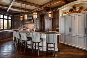 Dual tone kitchen with a breakfast bar area, dark stone counters, coffered ceiling, decorative light fixtures, and dual tone cabinetry
