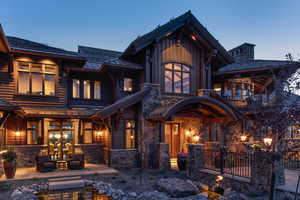 Back of house at dusk with stone siding, french doors, and a balcony