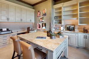 Kitchen featuring light stone countertops, a breakfast bar area, a center island, open shelves, and white cabinetry
