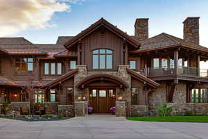 View of front of home with stone siding, a chimney, and a balcony