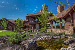 Back of house with a balcony, stone siding, a garden pond, and a chimney