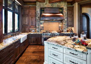 Kitchen featuring two tone color scheme, light stone counters, dark wood-style flooring, range with two ovens, and ventilation hood