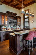 Indoor wet bar with glass insert cabinets, dark wood finish cabinets, a high wood beamed ceiling, dark wood-style floors, and decorative light fixtures