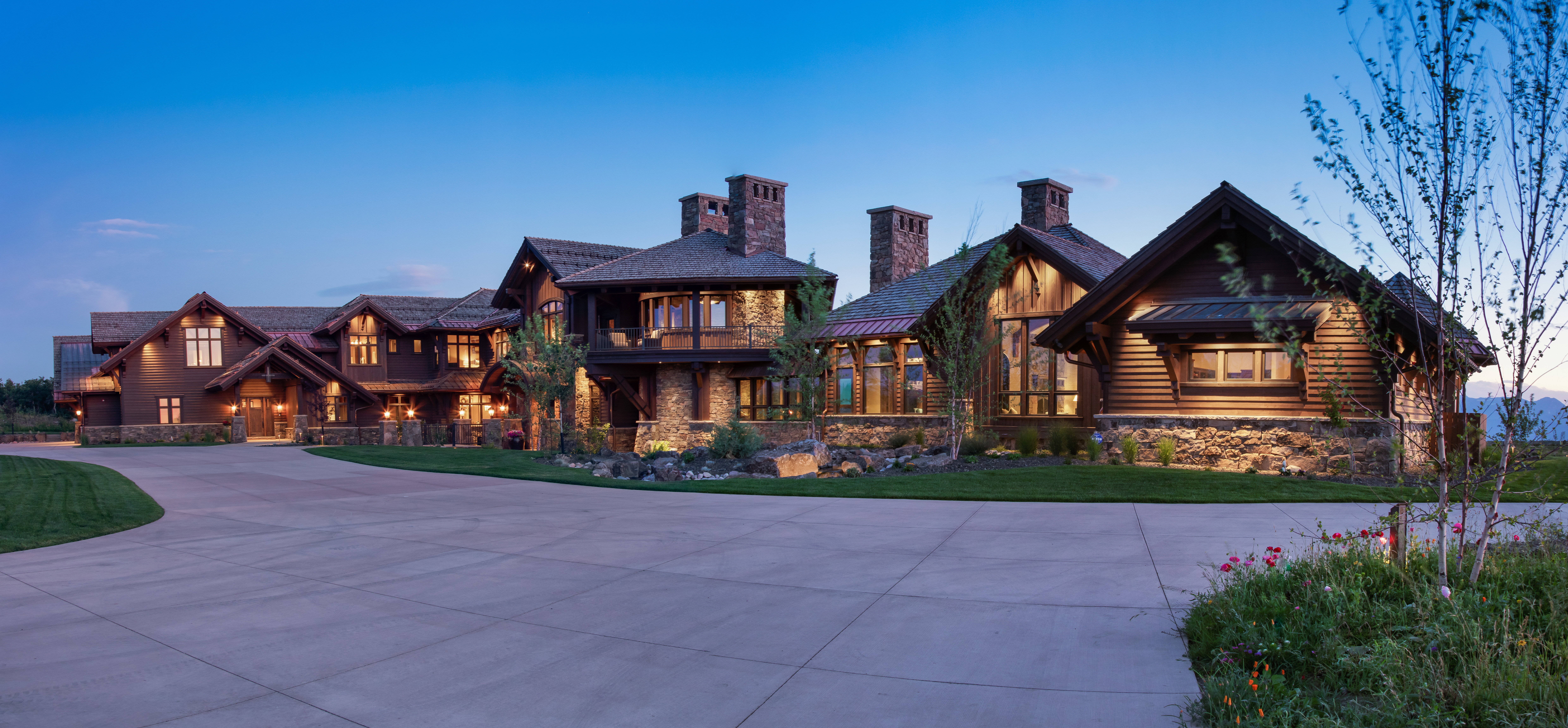 View of front facade featuring stone siding, a balcony, curved driveway, a chimney, and a front lawn