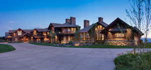View of front facade featuring stone siding, a balcony, curved driveway, a chimney, and a front lawn