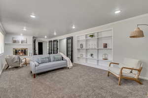 Carpeted living area with a glass covered fireplace, built in shelves, crown molding, and recessed lighting