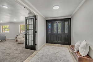 Entrance foyer with ornamental molding, light tile patterned floors, and light carpet