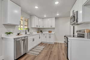 Kitchen featuring stainless steel appliances, white cabinetry, light wood-style floors, recessed lighting, and light stone countertops