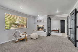 Living area featuring carpet flooring, french doors, a glass covered fireplace, crown molding, and recessed lighting