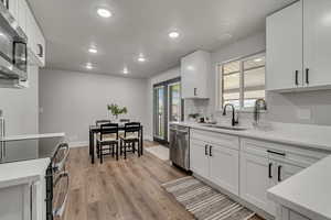 Kitchen featuring light stone countertops, white cabinets, stainless steel appliances, light wood-style flooring, and recessed lighting
