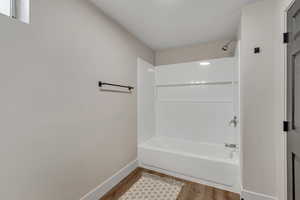 Bathroom with washtub / shower combination and wood finished floors