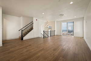 Unfurnished living room featuring dark wood-style flooring, a textured ceiling, and a chandelier