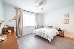 Bedroom with a wainscoted wall, wood finished floors, and ceiling fan