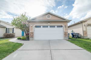 Single story home with stone siding, stucco siding, a front lawn, and concrete driveway