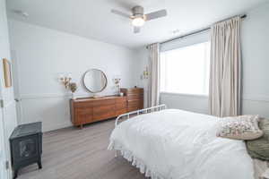 Bedroom with wainscoting, a wood stove, light wood-style floors, and a ceiling fan