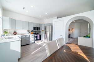 Kitchen featuring stainless steel appliances, light wood-style flooring, gray cabinets, arched walkways, and recessed lighting