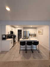 Kitchen featuring decorative backsplash, stainless steel appliances, white cabinets, a breakfast bar, and recessed lighting