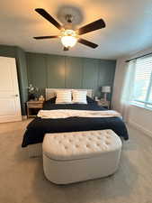 Bedroom featuring a decorative wall, a textured ceiling, light carpet, and a ceiling fan