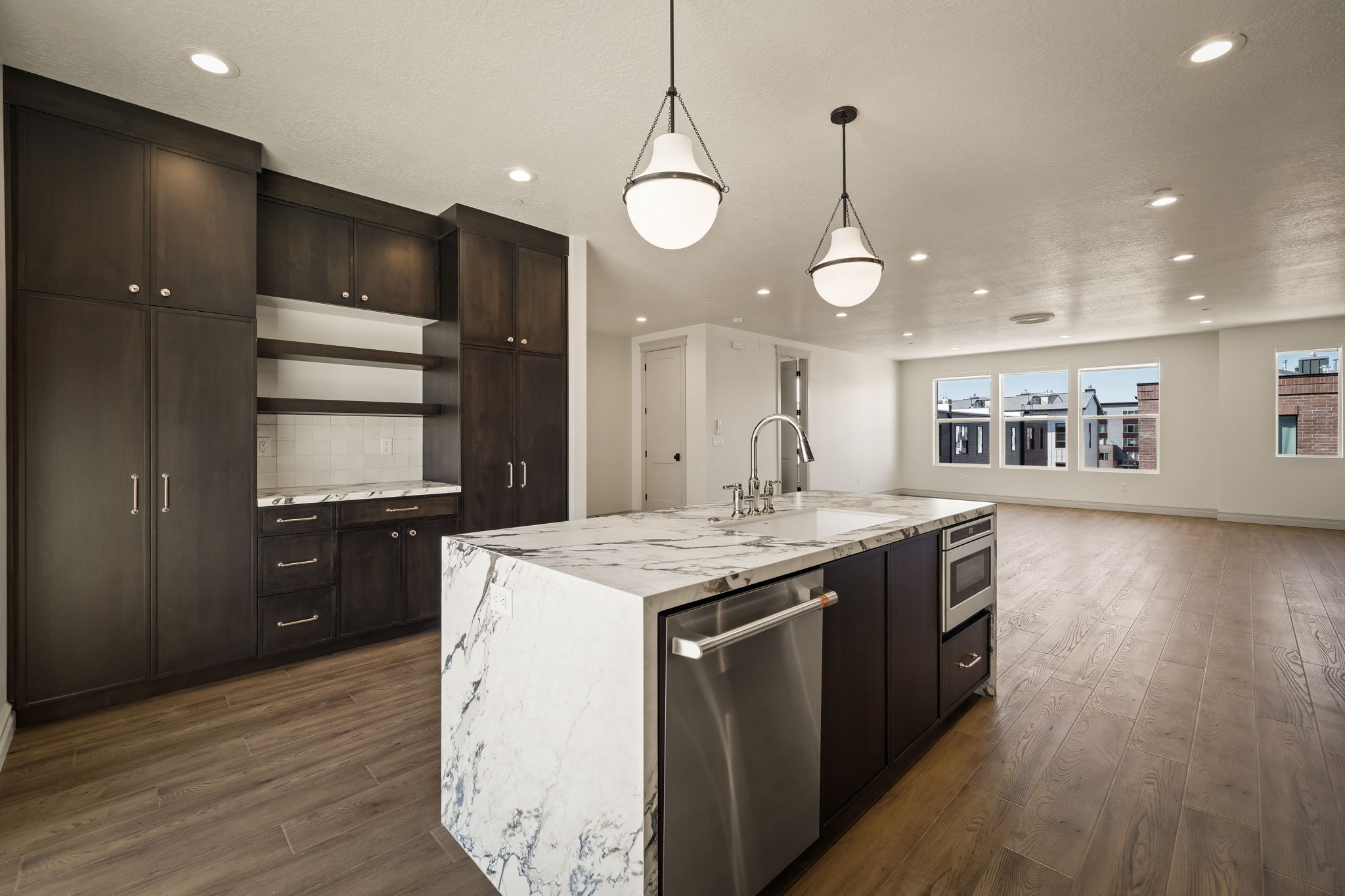 Kitchen with stainless steel appliances, light stone countertops, a kitchen island with sink, dark wood finished floors, and tasteful backsplash