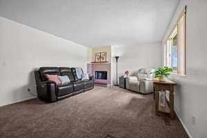 Living area with carpet flooring, a textured ceiling, and a brick fireplace
