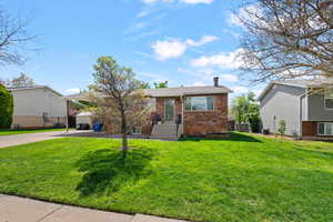 View of front facade with brick siding, driveway, a carport, a front yard, and a chimney