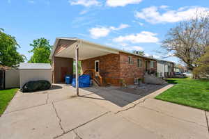 View of side of property with a yard, driveway, a storage shed, a carport, and brick siding