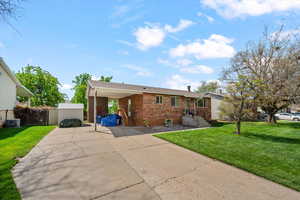 Ranch-style house with a front yard, brick siding, a carport, and driveway