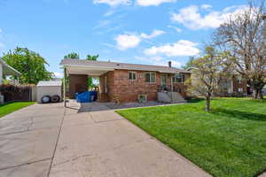 Single story home featuring brick siding, a front yard, a carport, and driveway