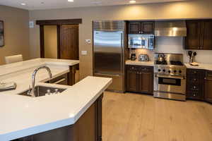Kitchen featuring stainless steel appliances, dark wood finish cabinetry, light wood-style flooring, light stone countertops, and recessed lighting