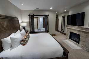 Bedroom featuring carpet, a stone fireplace, recessed lighting, and ensuite bathroom