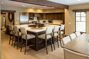 Kitchen with a kitchen breakfast bar, recessed lighting, dark wood finish cabinetry, light wood-style flooring, and beamed ceiling