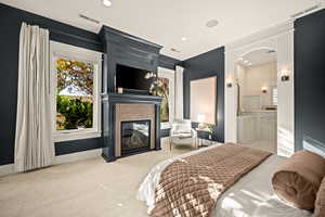Bedroom with arched walkways, light carpet, a glass covered fireplace, recessed lighting, and ensuite bath