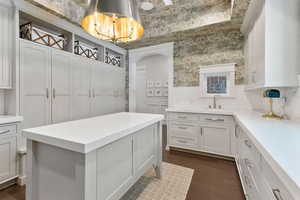 Kitchen featuring wallpapered walls, white cabinets, dark wood-style flooring, a kitchen island, and light stone counters