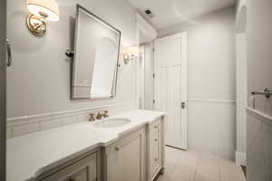 Bathroom featuring tile walls, vanity, a wainscoted wall, and light tile patterned floors