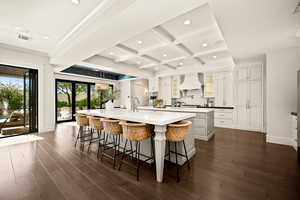 Kitchen featuring coffered ceiling, a kitchen breakfast bar, dark wood-style floors, backsplash, and white cabinets