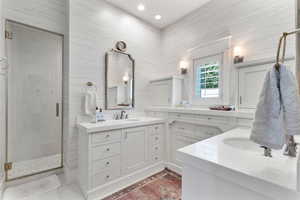 Bathroom featuring two vanities, a stall shower, recessed lighting, and tile walls