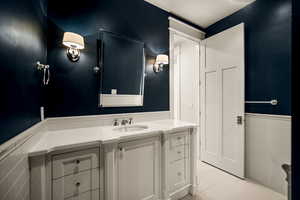 Bathroom featuring a wainscoted wall, tile walls, vanity, and light tile patterned flooring