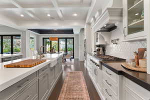 Kitchen featuring coffered ceiling, stainless steel appliances, dark stone countertops, glass fronted cabinets, and dark wood-style floors