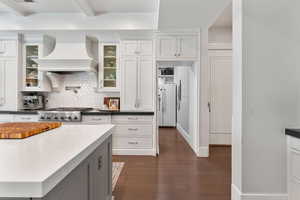 Dual tone kitchen featuring dark wood-style floors, decorative backsplash, glass fronted cabinets, stainless steel gas stovetop, and high end white fridge