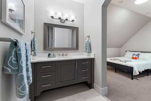 Ensuite bathroom featuring vanity, light carpet, and vaulted ceiling
