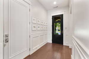 Entryway featuring dark wood-style flooring, a decorative wall, wainscoting, and recessed lighting