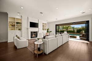 Living room with ornamental molding, built in features, dark wood finished floors, a glass covered fireplace, and recessed lighting