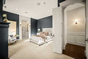 Bedroom with arched walkways, recessed lighting, ensuite bathroom, wood finished floors, and a wainscoted wall