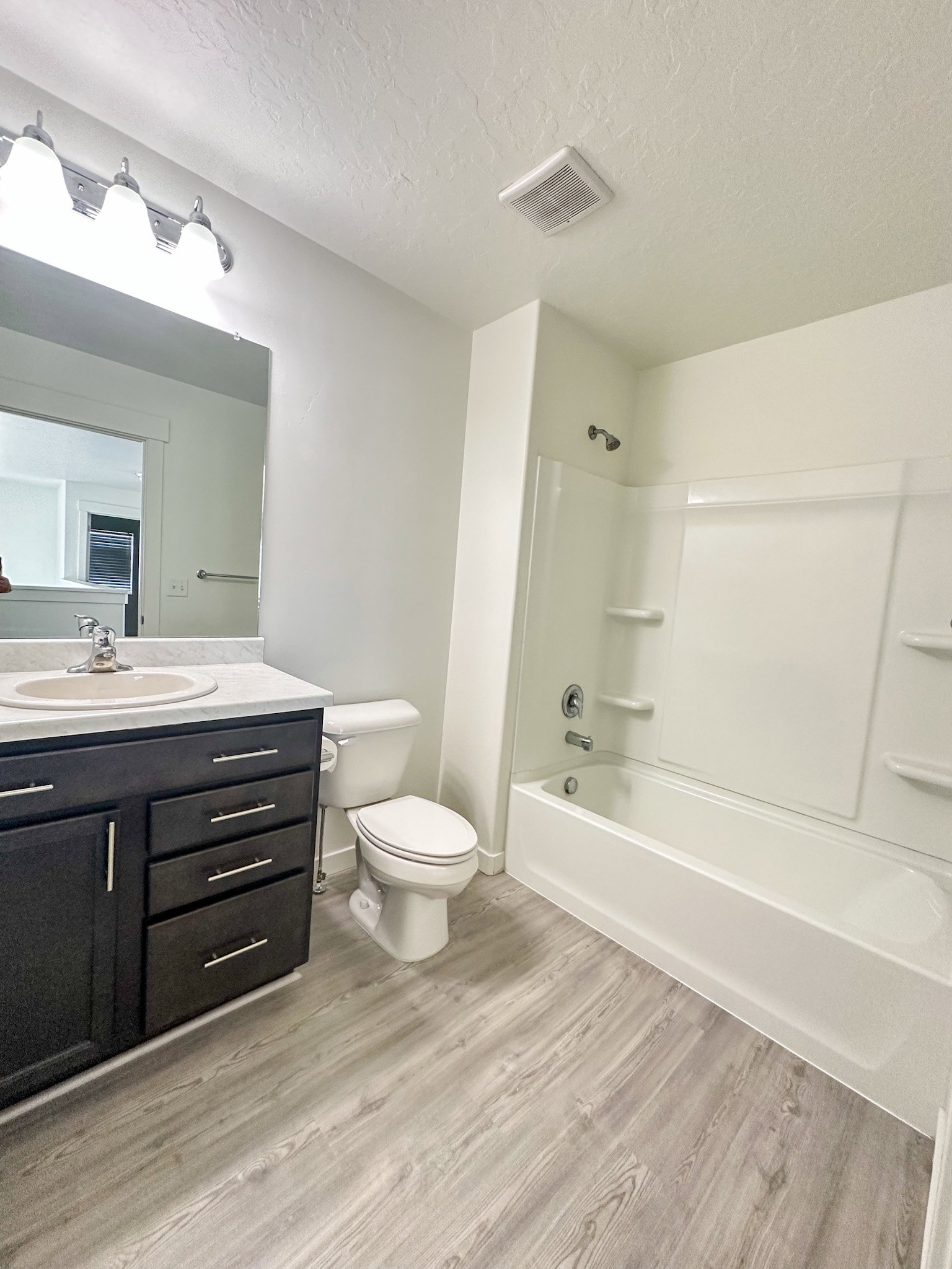 Full bathroom with vanity, light wood-style flooring,  shower combination, and a textured ceiling
