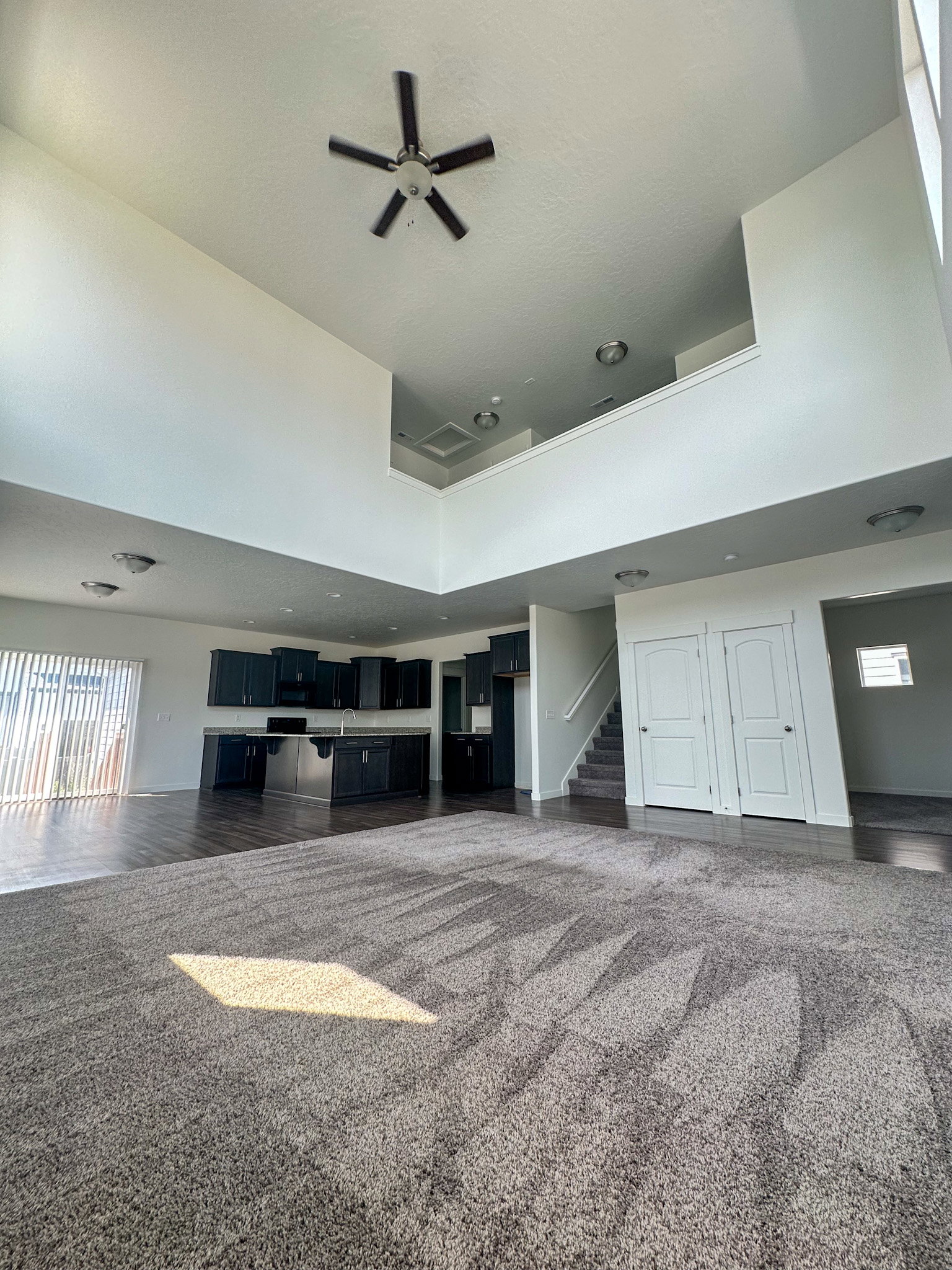 Unfurnished living room with dark carpet, a high ceiling, and a ceiling fan