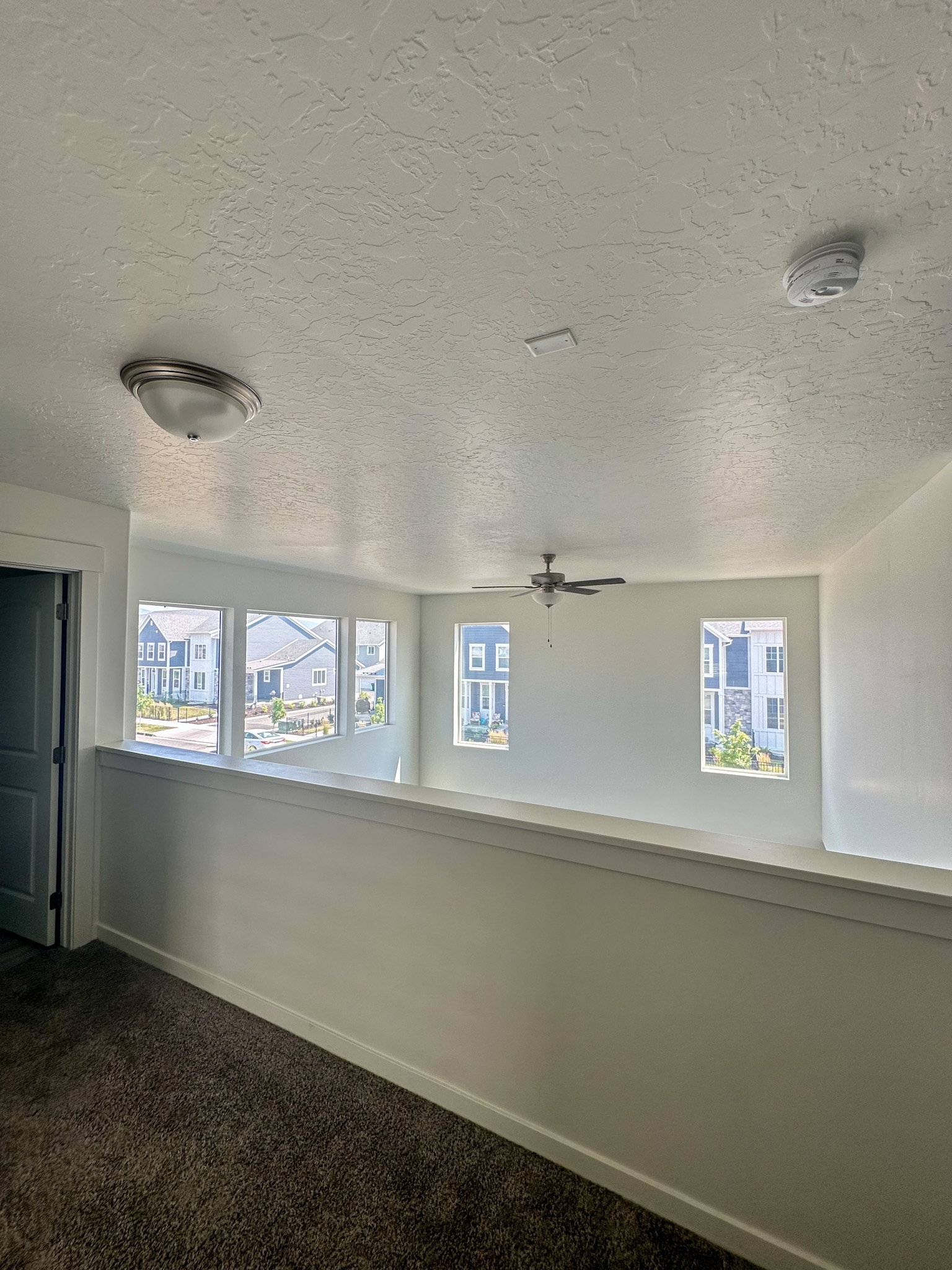 Carpeted empty room featuring a textured ceiling, a smoke detector, and ceiling fan