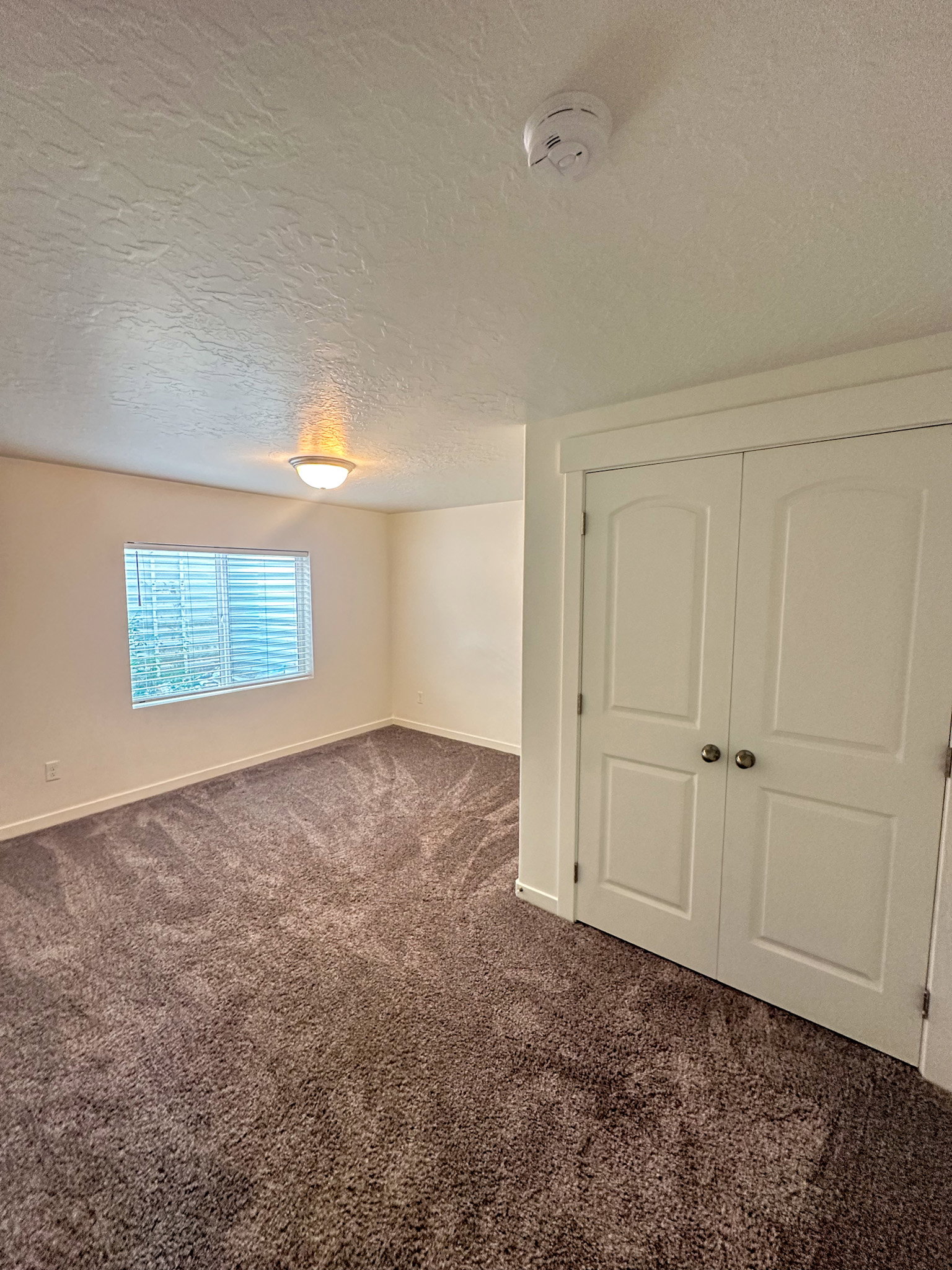 Unfurnished room with dark carpet, a textured ceiling, and a smoke detector