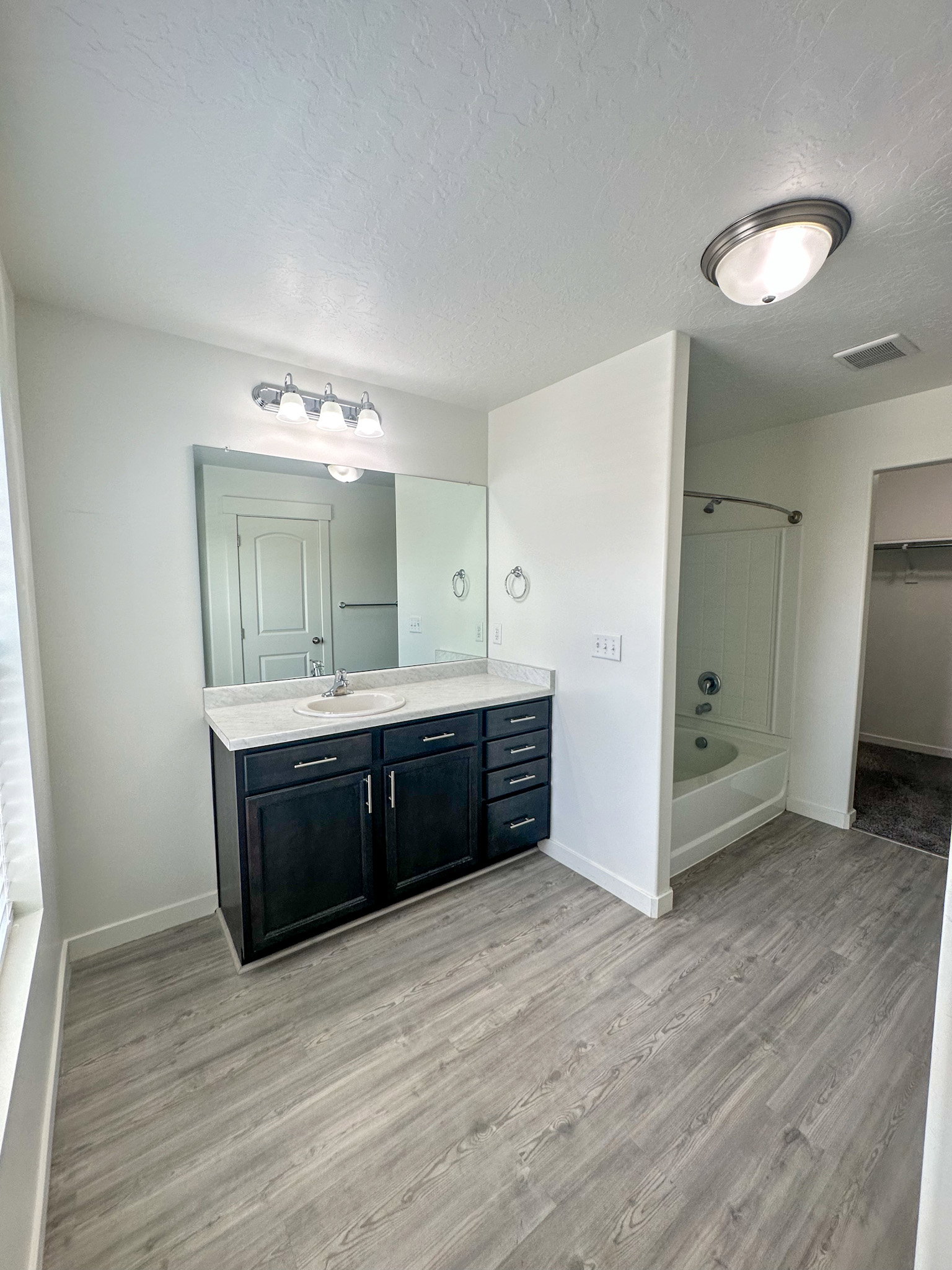 Full bath featuring vanity, light wood-style floors, a textured ceiling,  shower combination, and a spacious closet