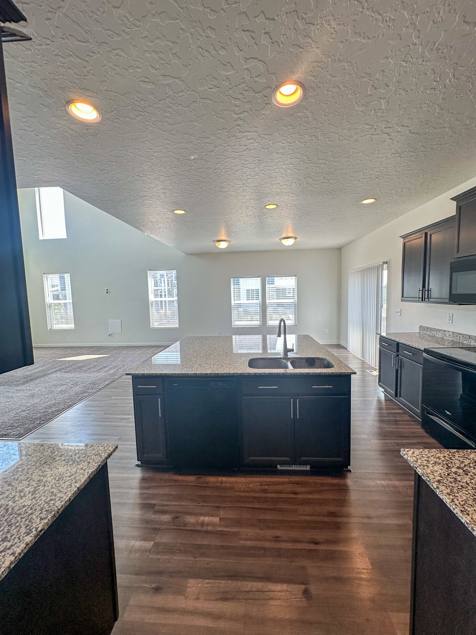 Kitchen featuring light stone countertops, a kitchen island with sink, black appliances, dark wood-type flooring, and a textured ceiling